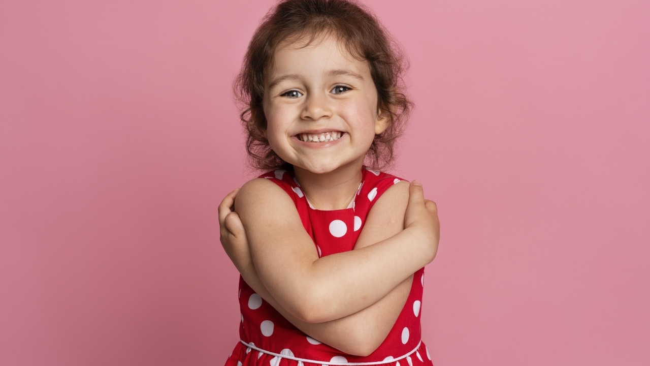 Улыбающаяся маленькая девочка в красном платье на розовом фоне