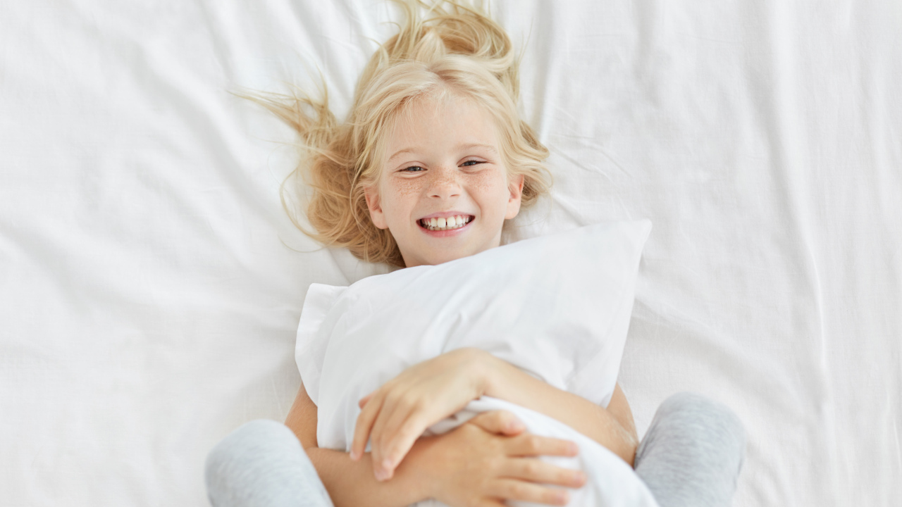 Улыбающаяся маленькая девочка с подушкой на кровати
