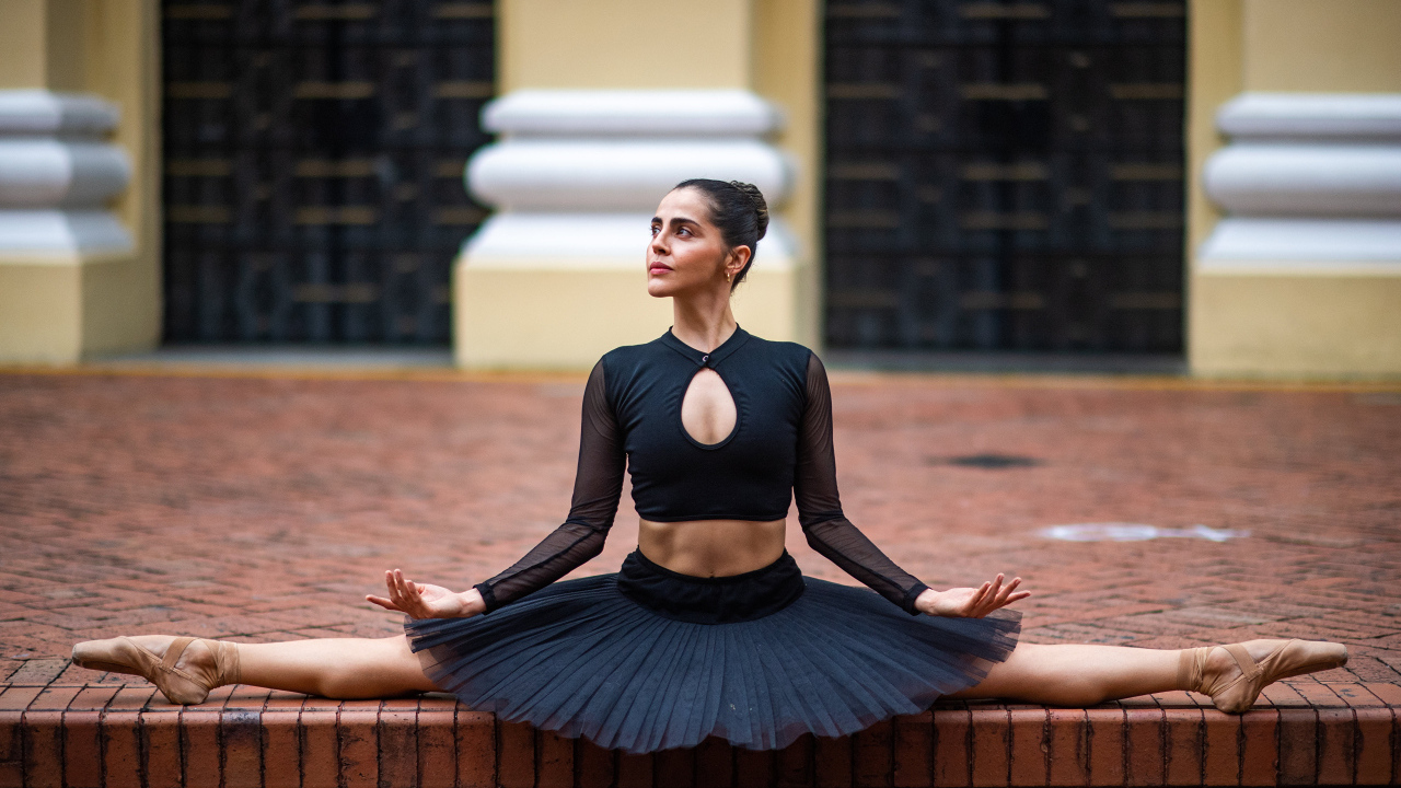 Девушка балерина в черном наряде сидит на шпагате