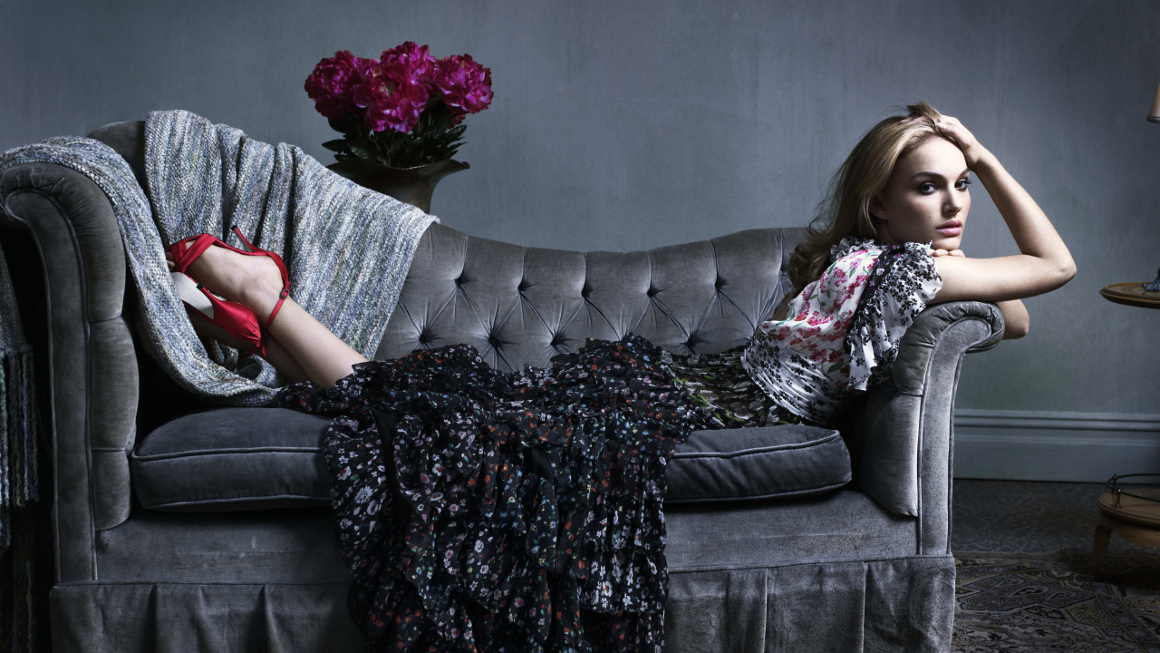 Актриса Натали Портман в платье лежит на сером диване