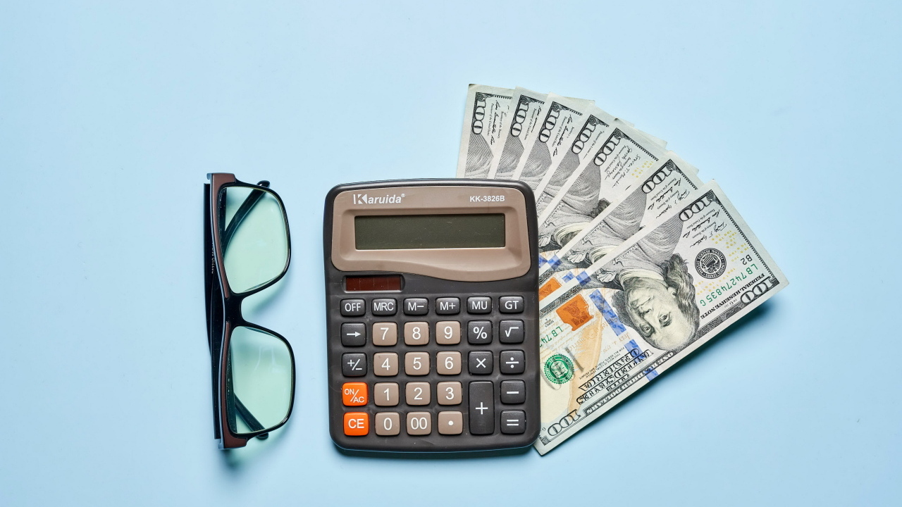 Очки, калькулятор и доллары на сером фоне