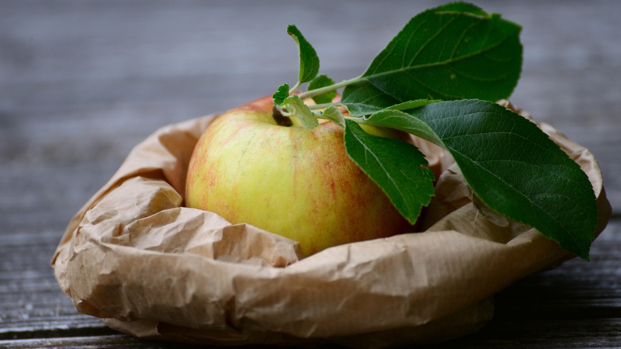 Яблоко с зелеными листьями на бумаге