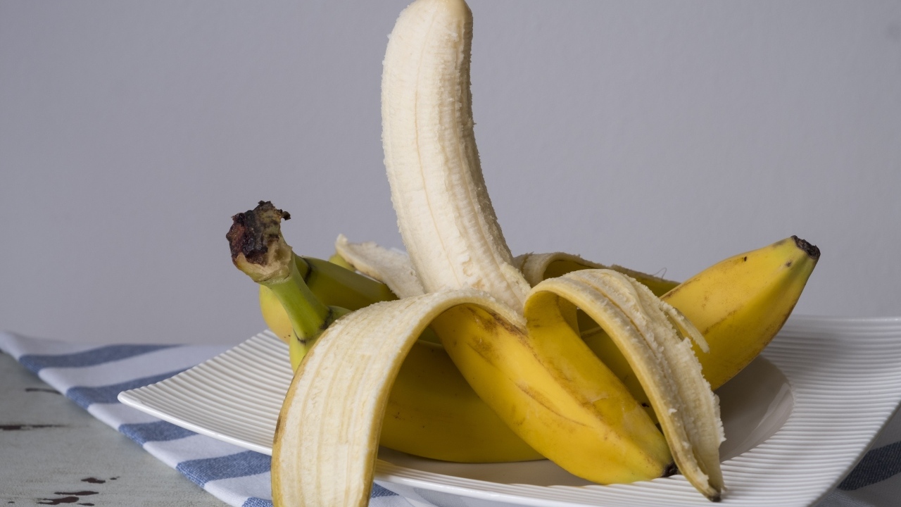 Очищенный банан на тарелке на сером фоне