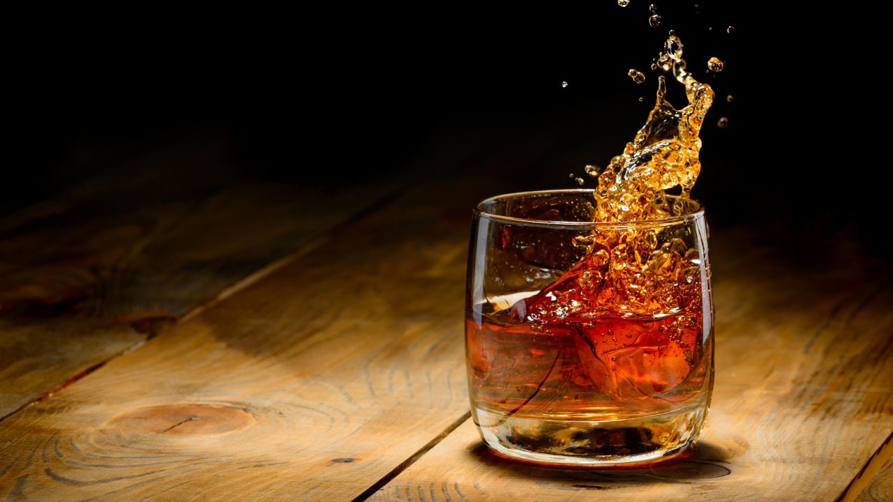 Брызги в стакане с виски со льдом на столе