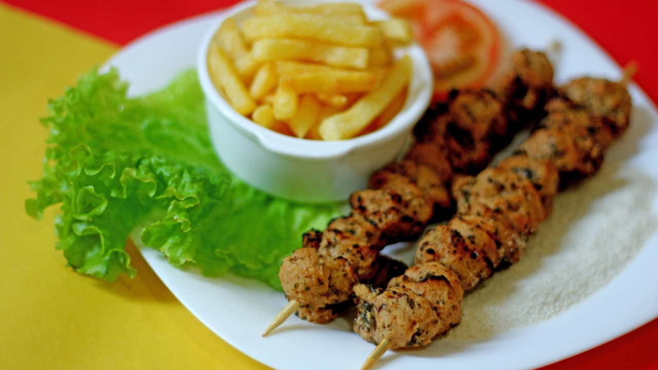 Шашлык на шпажках на столе с картофелем фри и листьями салата