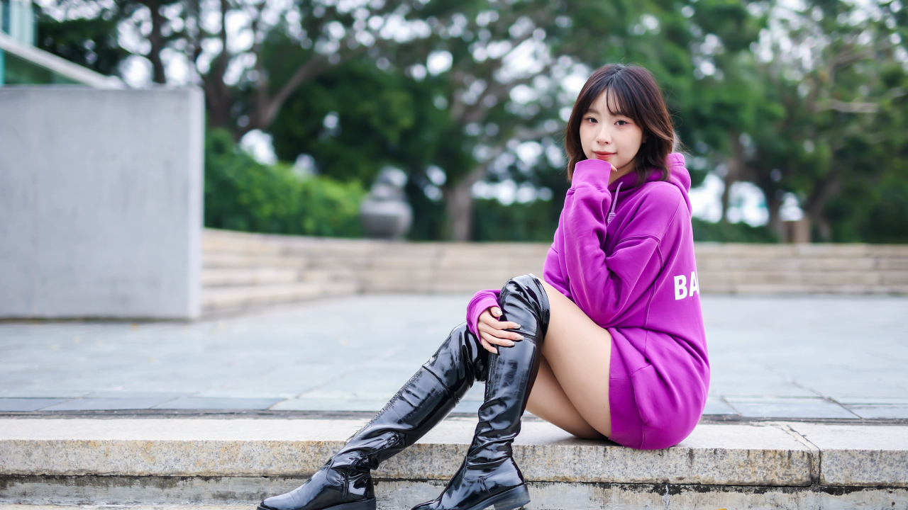 Девушка азиатка в длинных черных сапогах сидит на ступенях