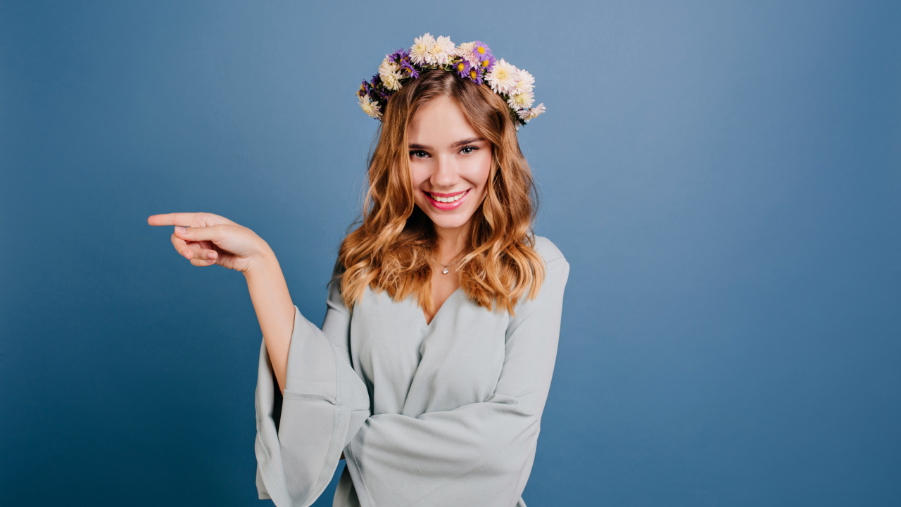 Милая улыбающаяся девушка с венком на голове на сером фоне