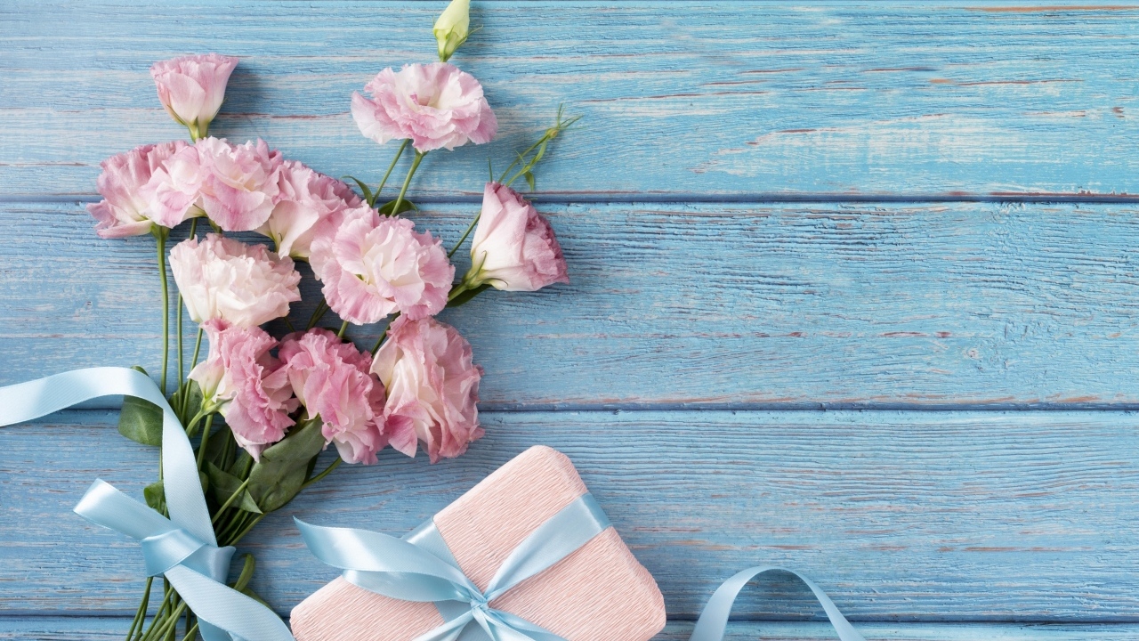 Букет розовых цветов эустомы с подарком на голубом столе