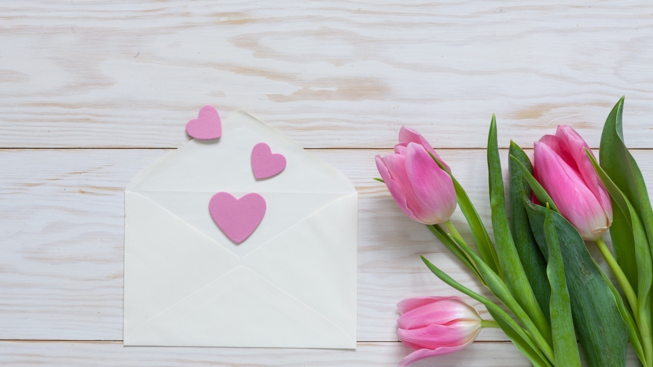 Розовые тюльпаны с конвертом с сердечками на деревянном фоне