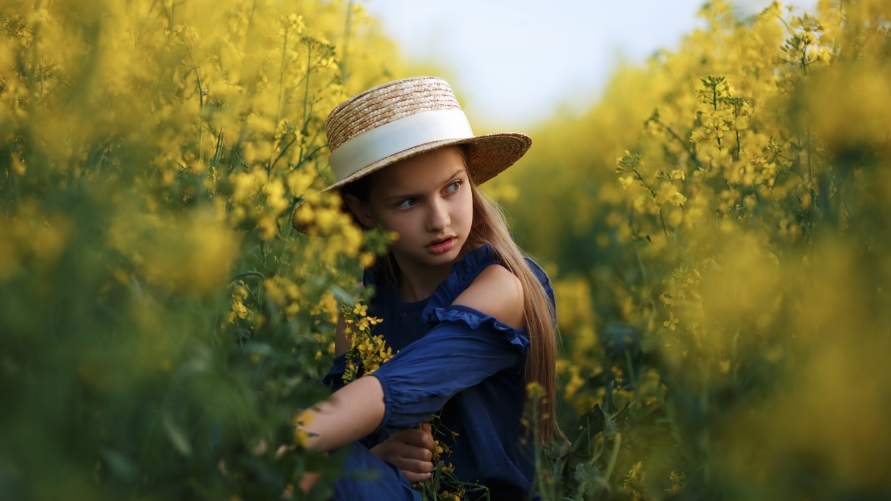 Девочка в шляпе на поле с желтыми цветами рапса