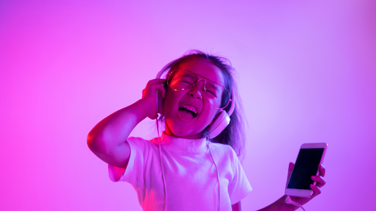 Маленькая девочка в наушниках с телефоном слушает музыку