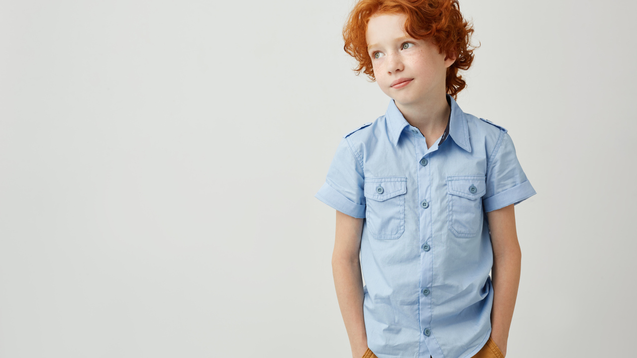 Рыжеволосый мальчик на фоне серой стены