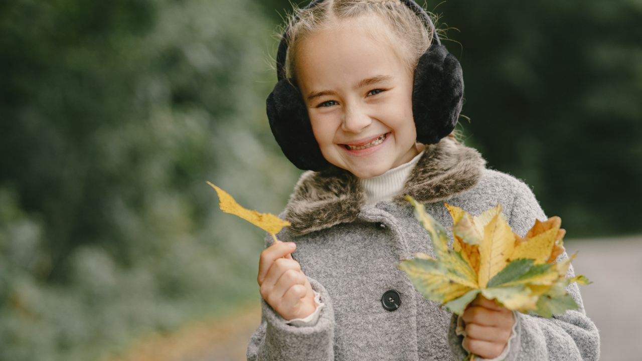 Улыбающаяся девочка с опавшими листьями в руках