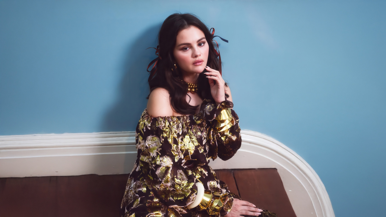 Актриса Селена Гомес на диване на фоне серой стены