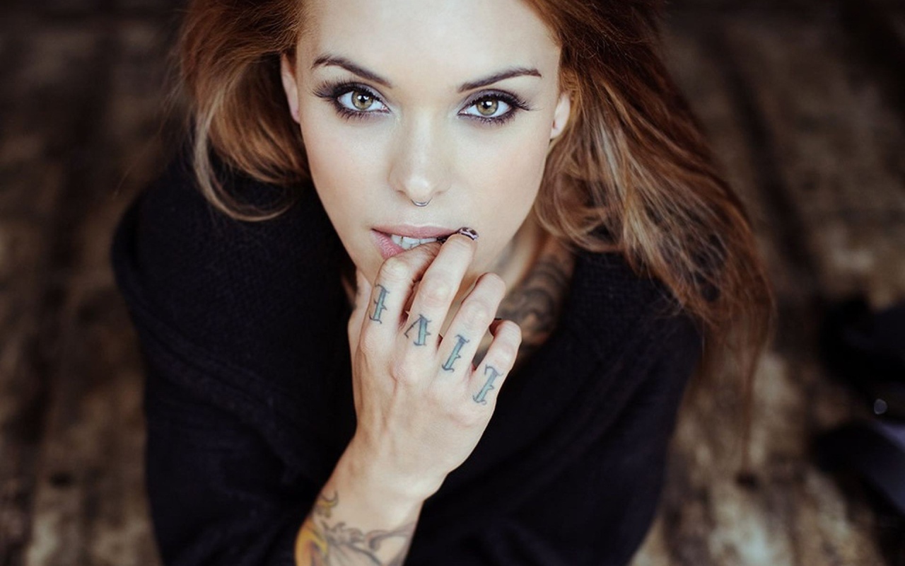 Девушка шатенка с пирсингом в носу и татуировкой на руке