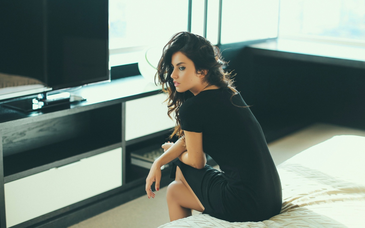 Девушка сидит на кровати перед телевизором