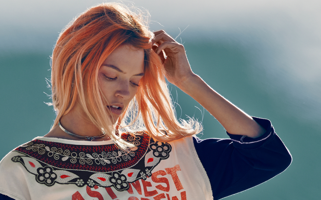 Рыжая девушка на ветру поправляет волосы