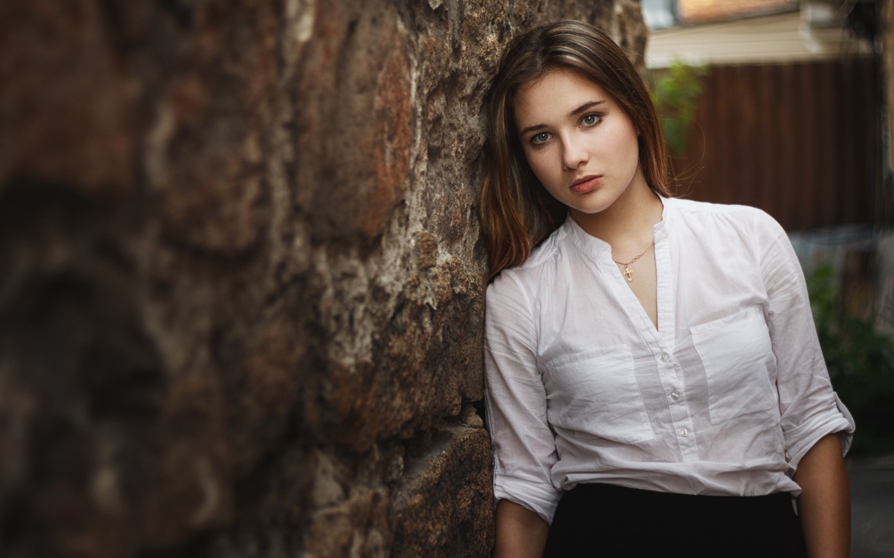 Девушка в белой рубашке стоит у стены