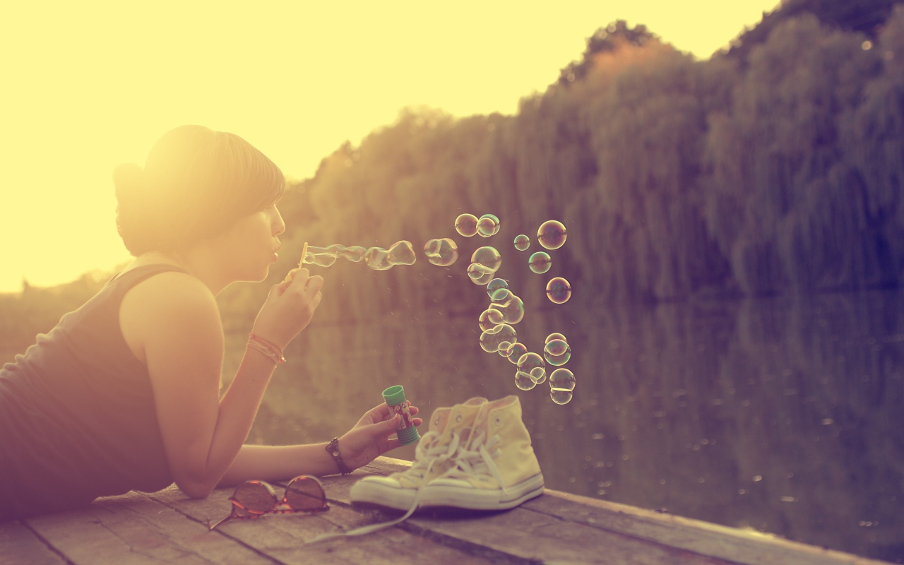 Девушка лежит на пирсе и играет с мыльными пузырями