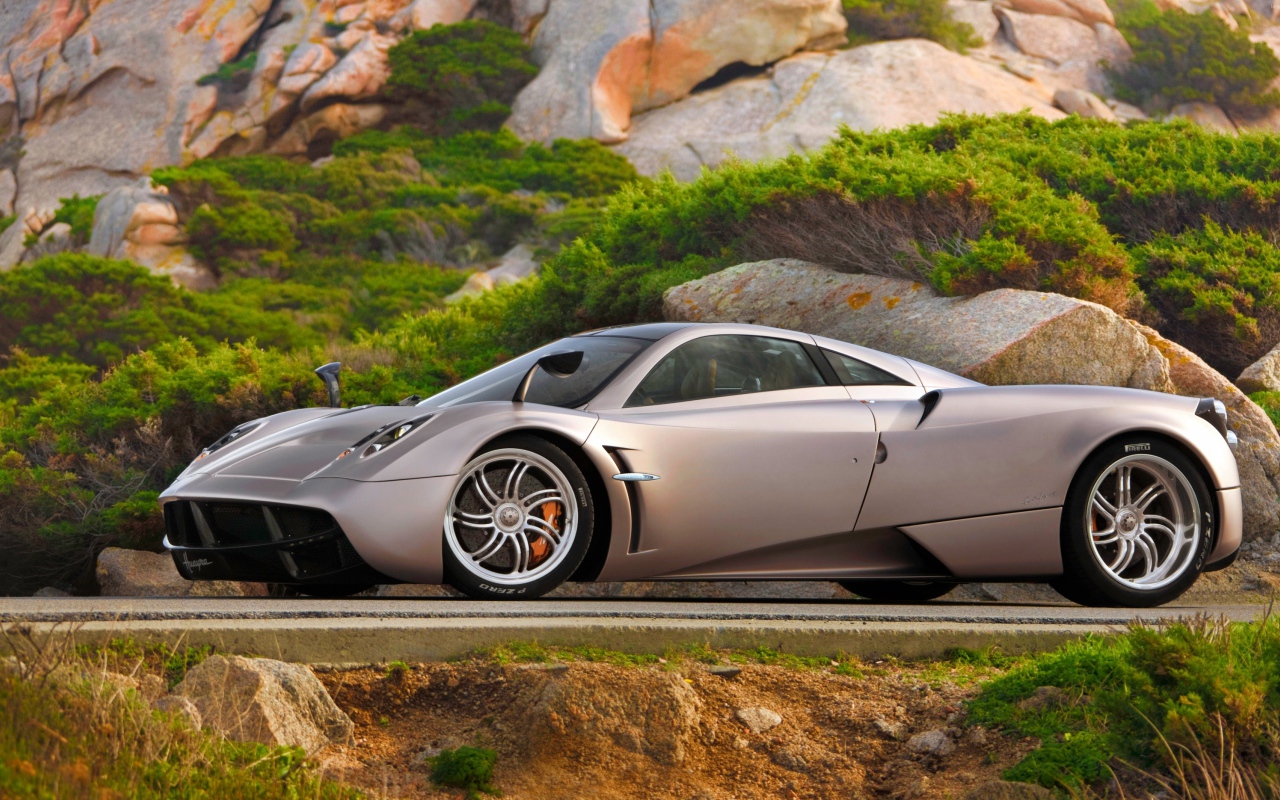 Серебристый быстрый автомобиль  Pagani Huayra на трассе у скалы