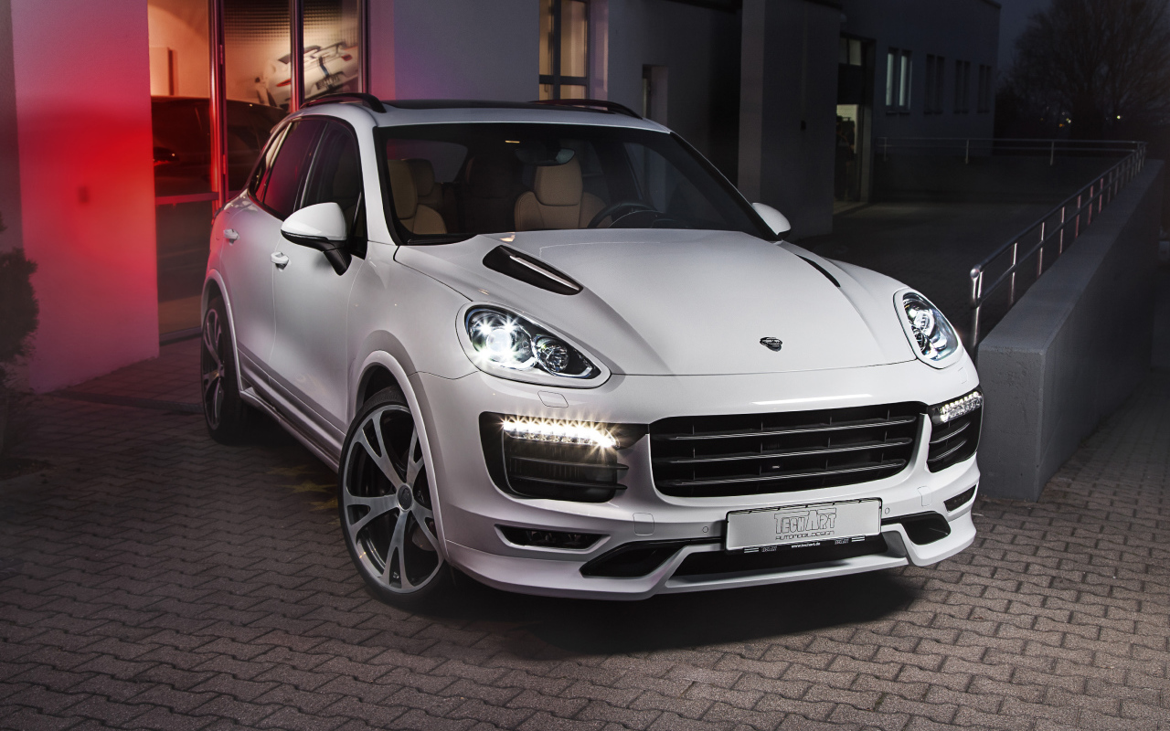 Белый внедорожник Porsche Cayenne с включенными фарами