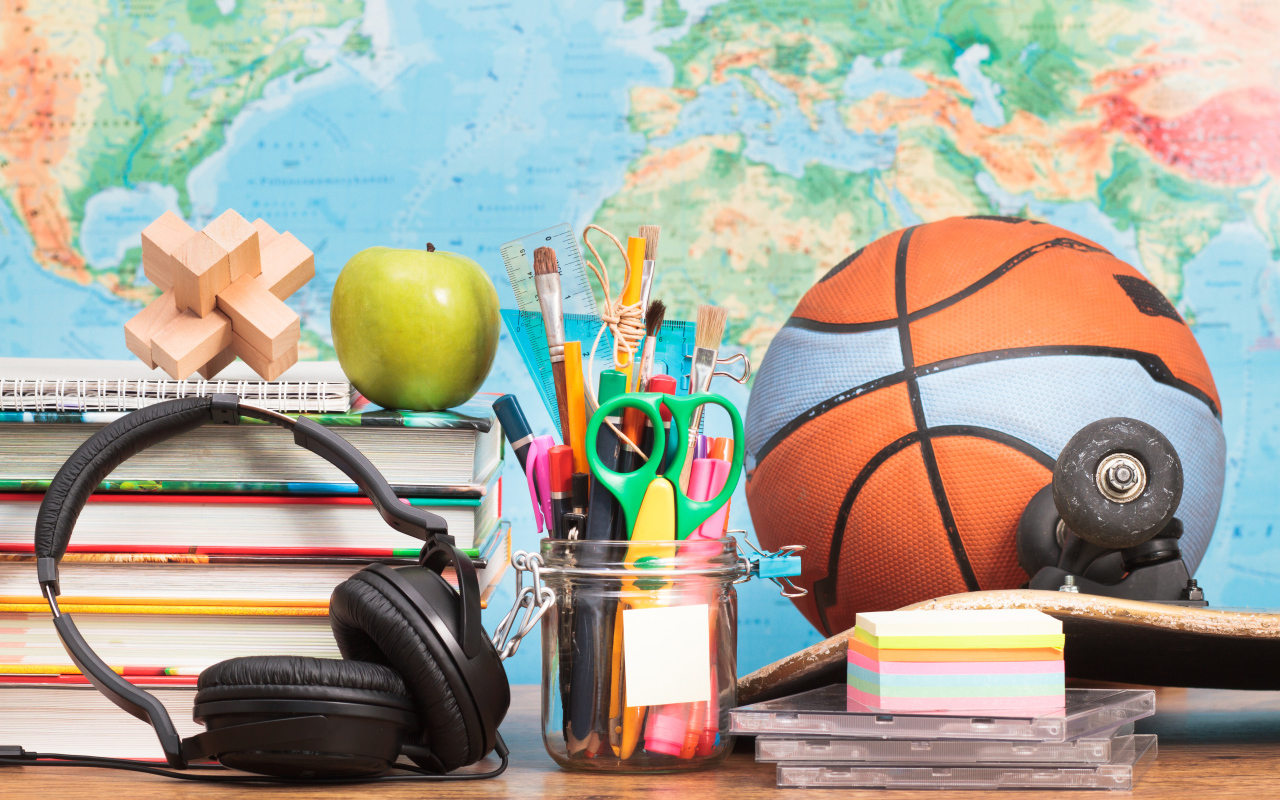 Мяч, наушники, книги и канцелярские принадлежности на столе на фоне карты