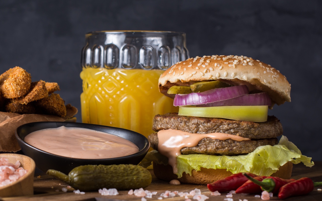 Аппетитный гамбургер на столе с соусом, овощами и соком