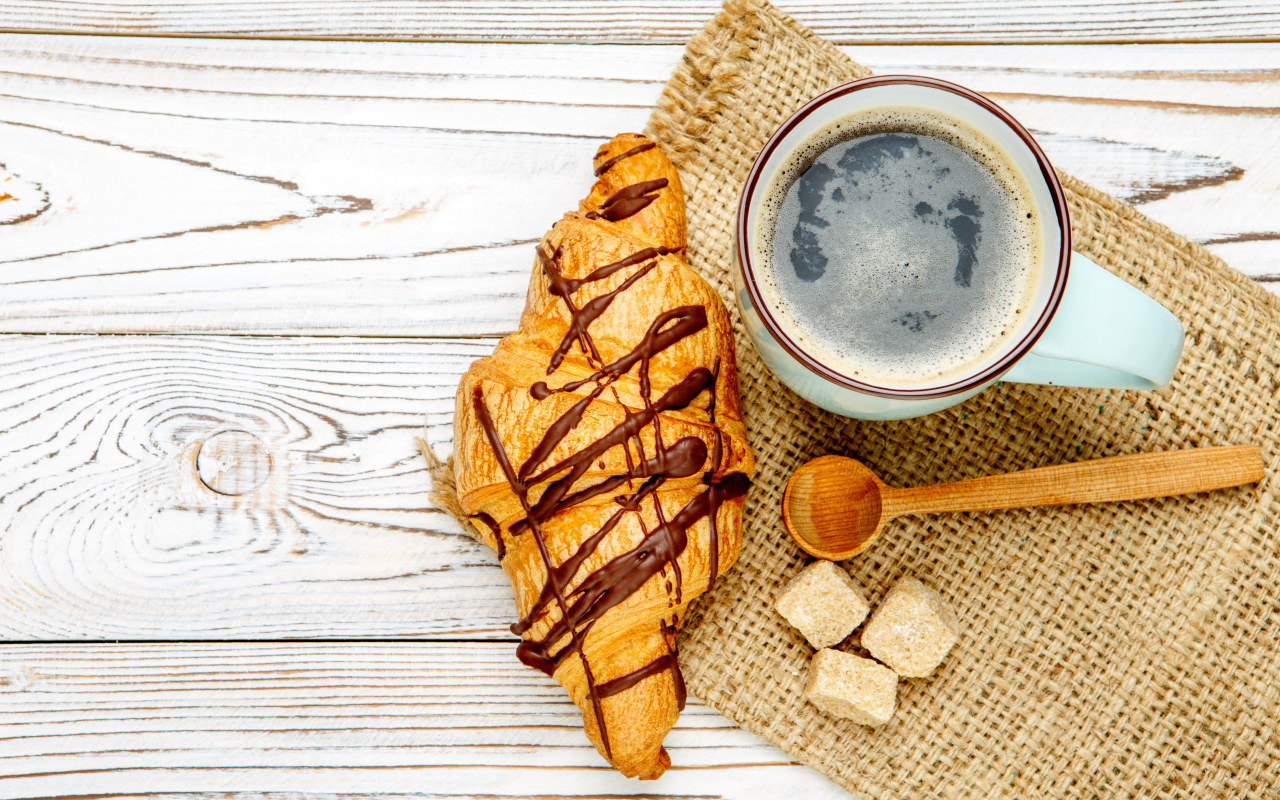 Круассан с шоколадом и чашкой кофе на столе