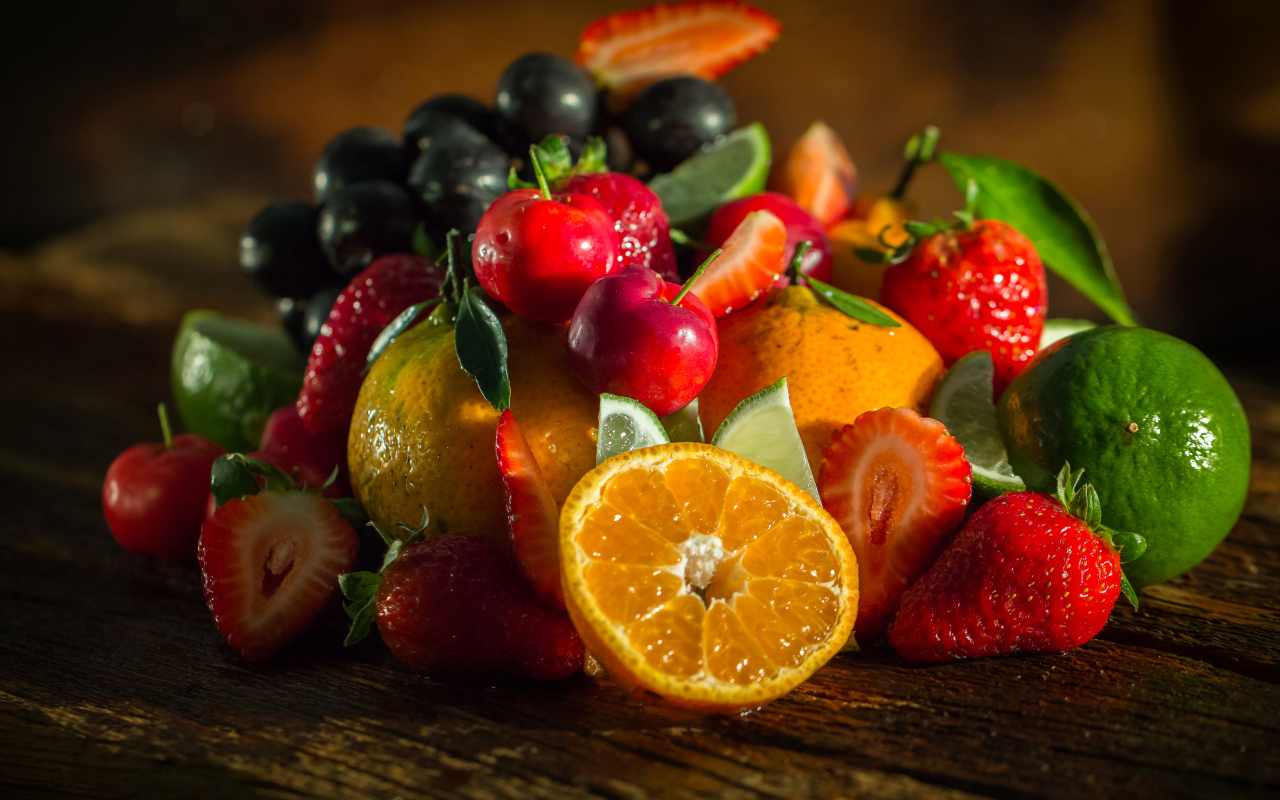 Свежие кусочки апельсина, лимона и ягоды вишни и клубники на столе