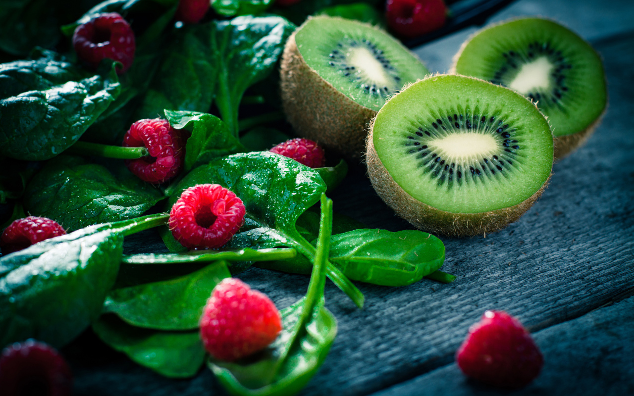 Половинки киви на столе с зелеными листьями и свежей малиной