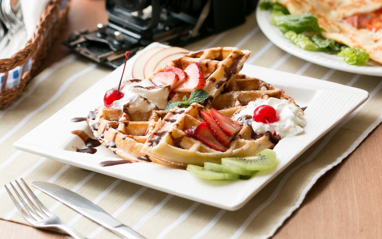 Сладкие вафли с ягодами клубники, вишни и кусочками киви на тарелке