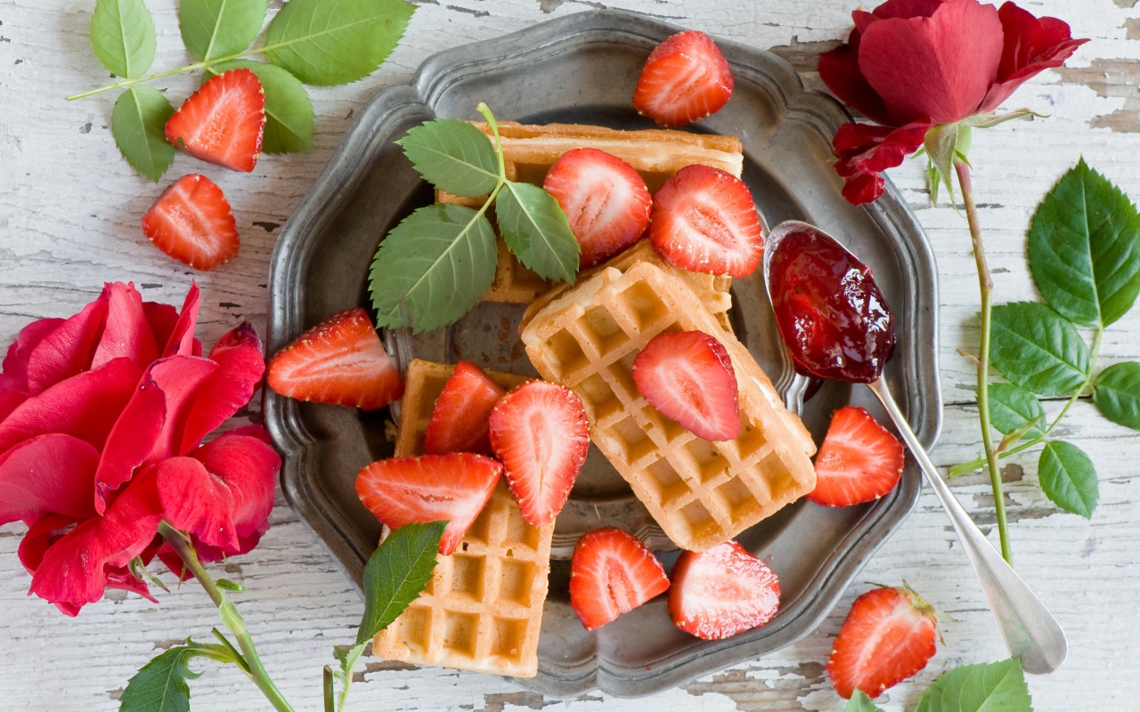 Сладкие вафли со свежей клубникой и красными розами на столе