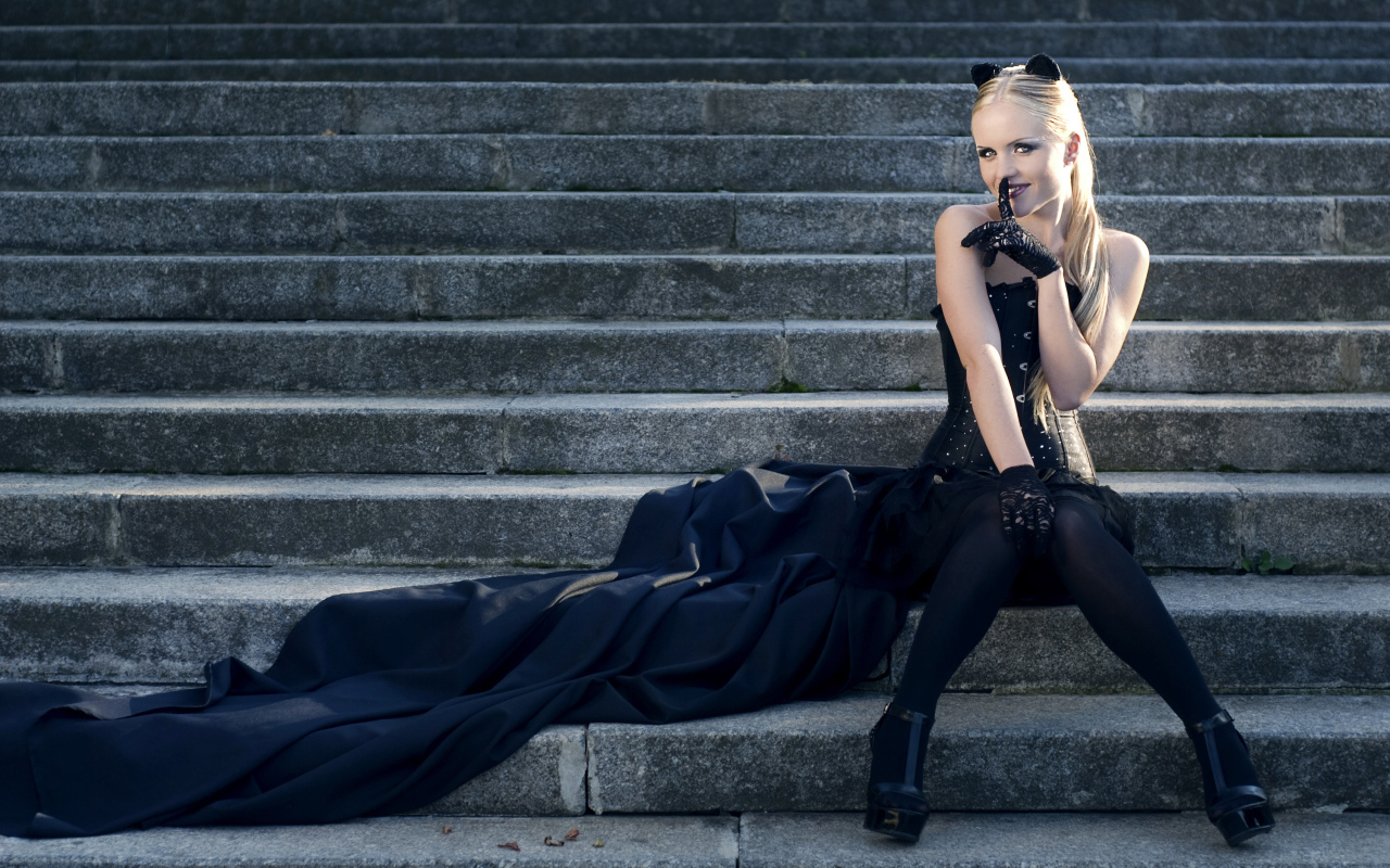 Красивая девушка блондинка  сидит на ступеньках в черном костюме