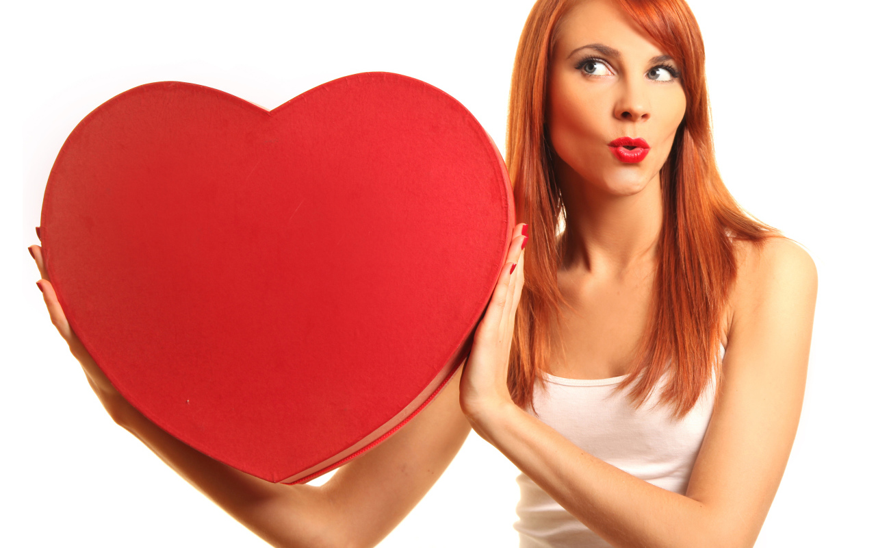 Рыжеволосая девушка с большим красным сердцем в руках на белом фоне