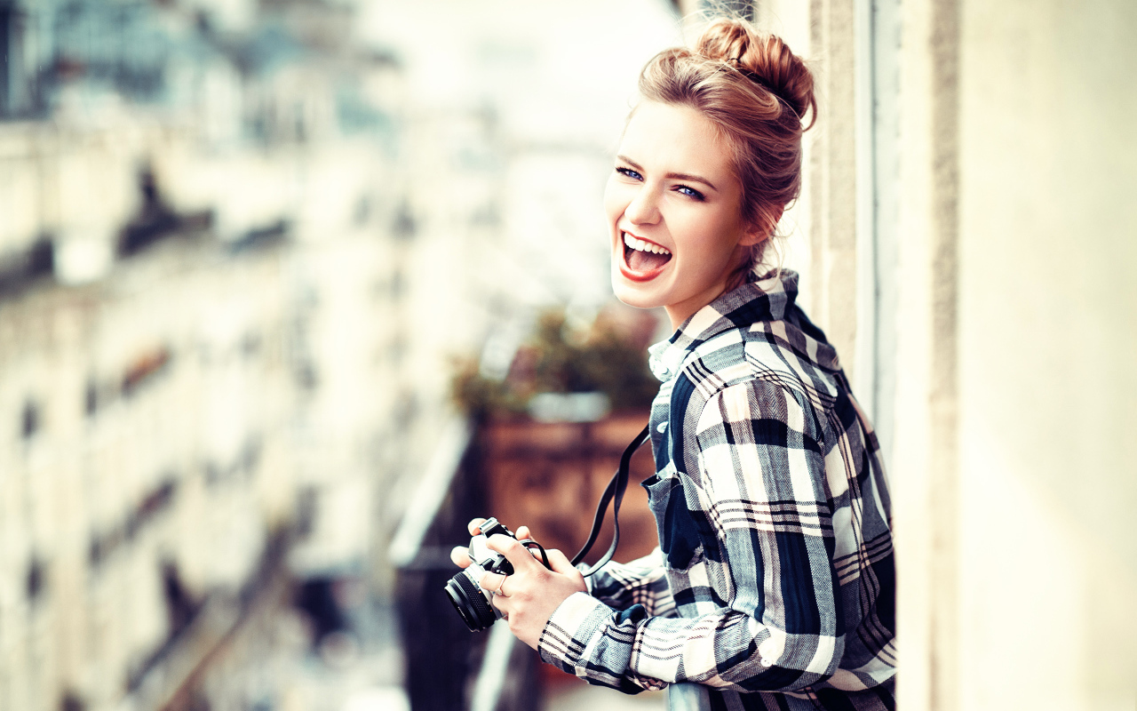 Улыбающаяся девушка в клетчатой рубашке с фотоаппаратом 