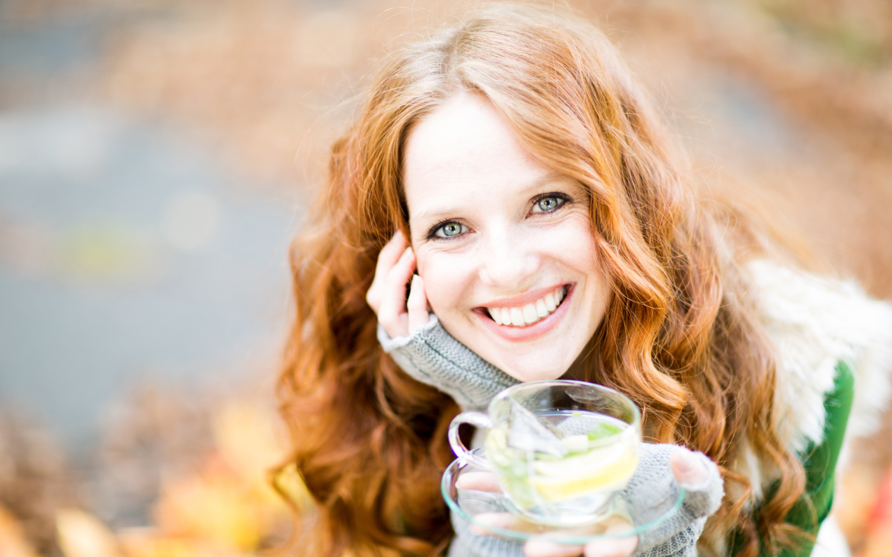 Улыбающаяся рыжеволосая девушка с чашкой чая в руке