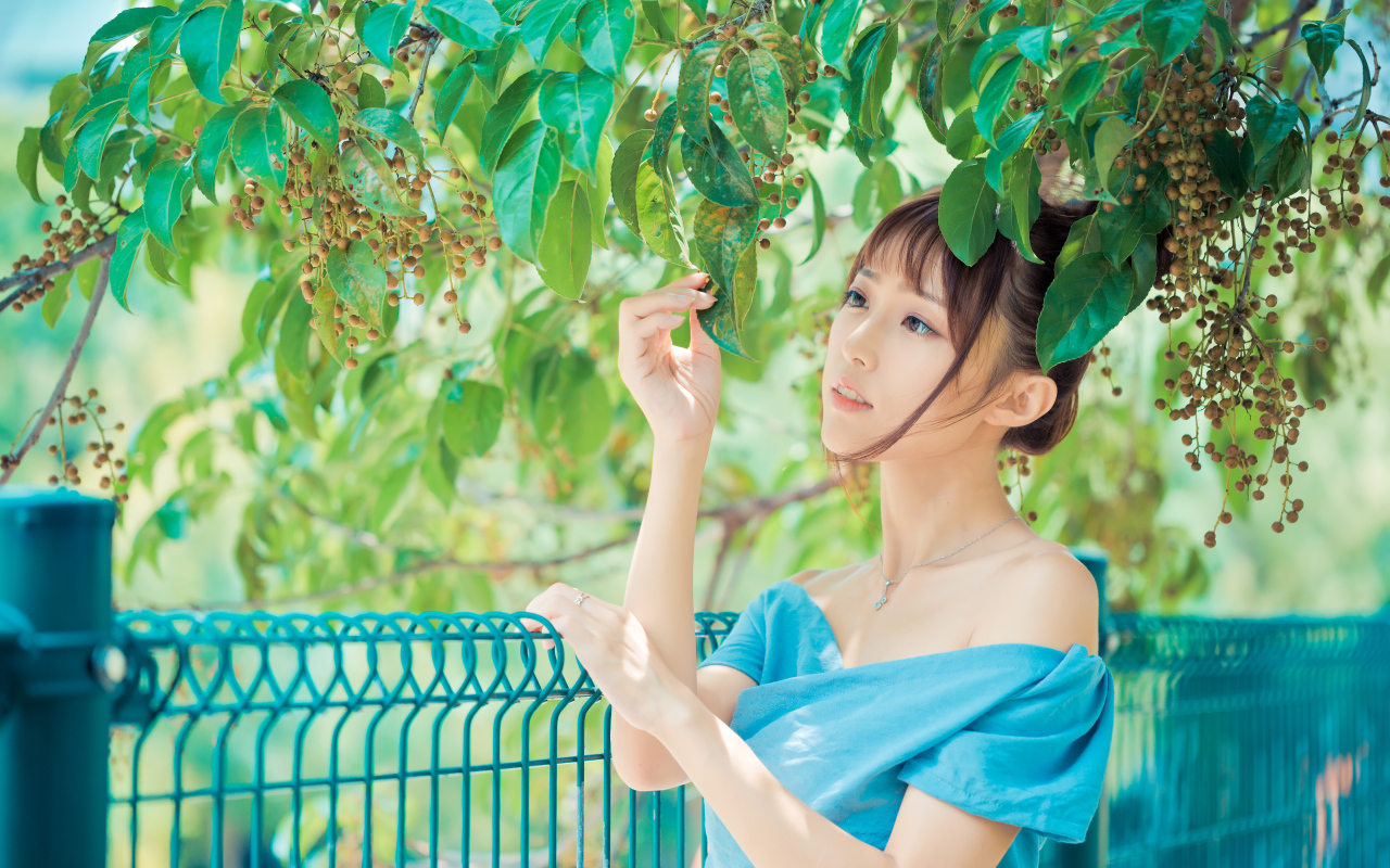 Молодая красивая девушка азиатка стоит у ветки с зелеными листьями