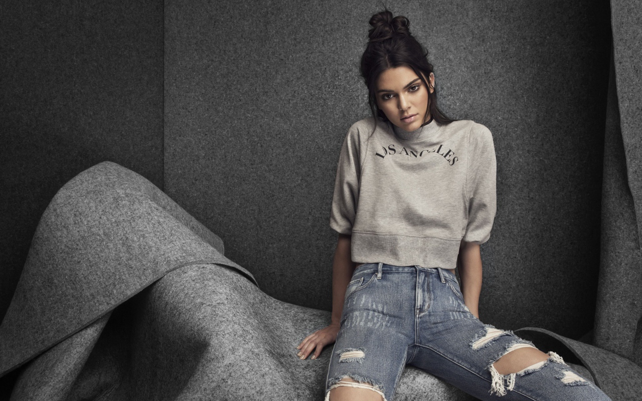 Модель Кендалл Дженнер в рваных джинсах на сером фоне