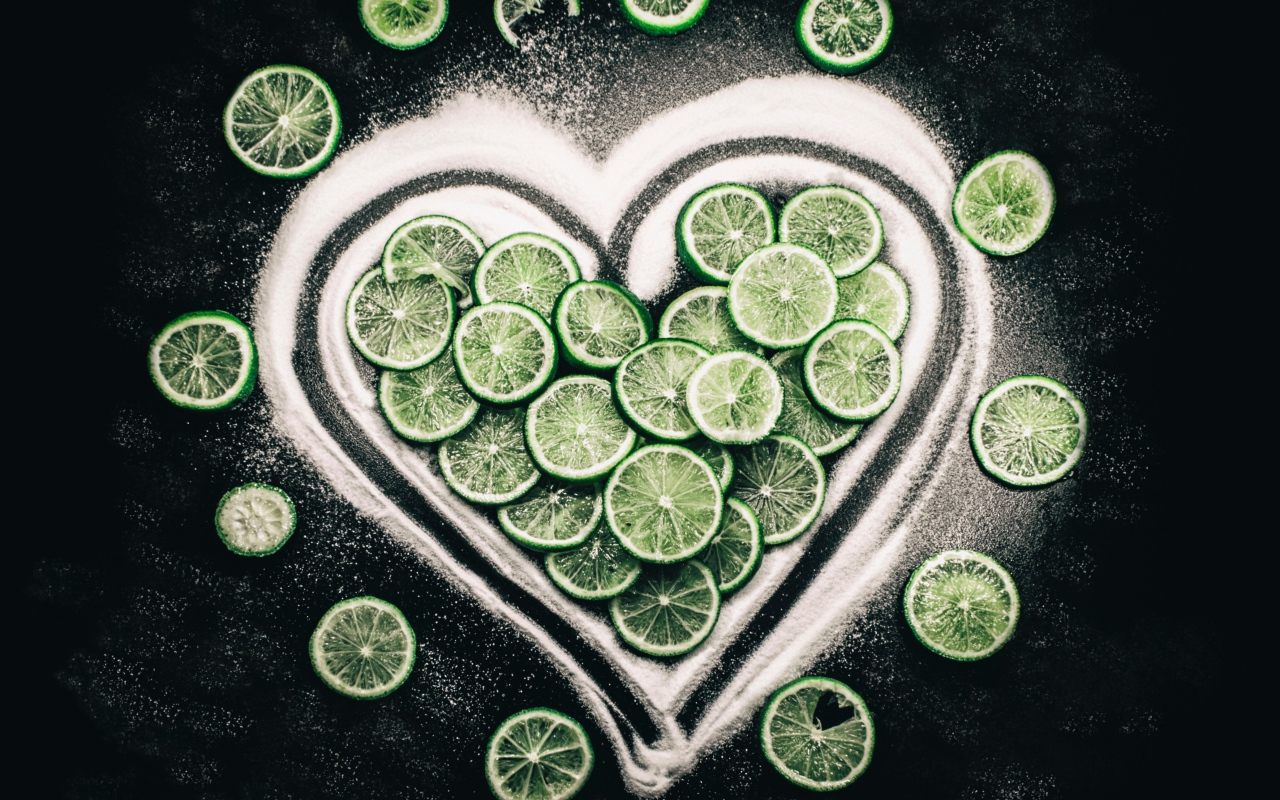 Сердце из сахара и кружочков  зеленого лайма на черном фоне