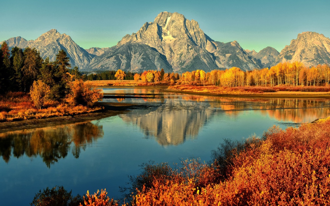 Горы и осенние деревья отражаются в реке 