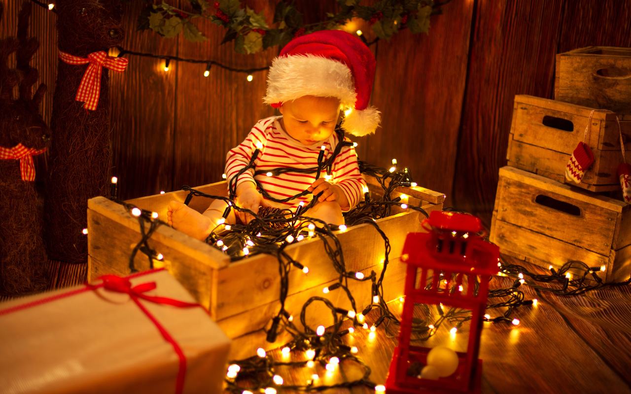 Маленький мальчик сидит в коробке с новогодней гирляндой
