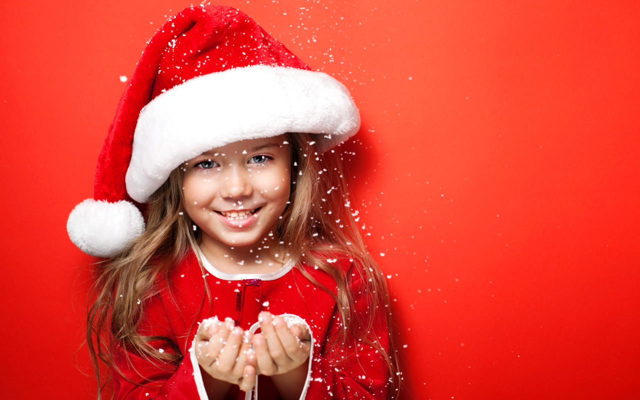 Маленькая девочка в новогодней шапке ловит руками снежинки