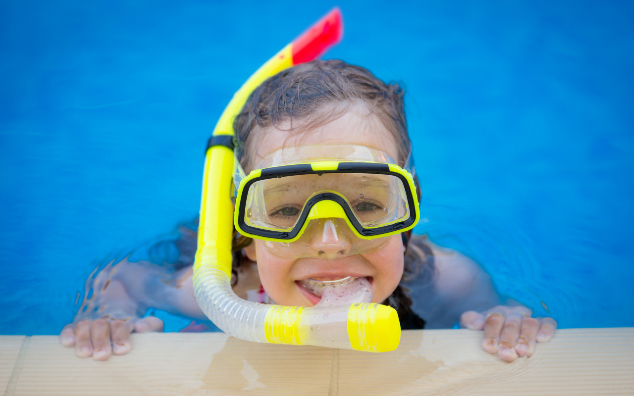 Маленькая девочка в маске с трубкой плавает в бассейне
