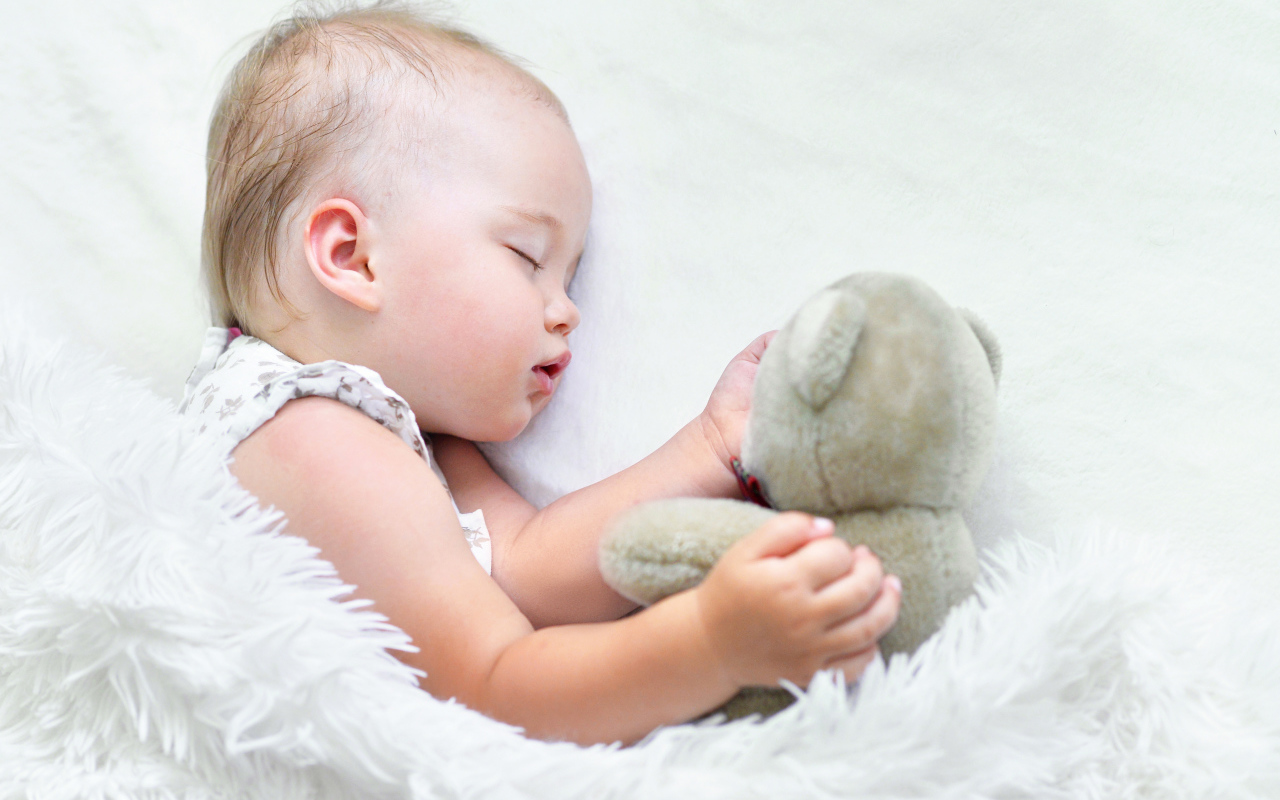 Маленькая девочка спит с мягкой игрушкой под белым одеялом