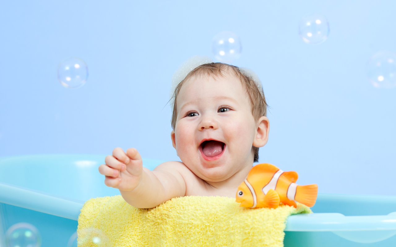 Веселый малыш купается в ванной с игрушечной рыбкой