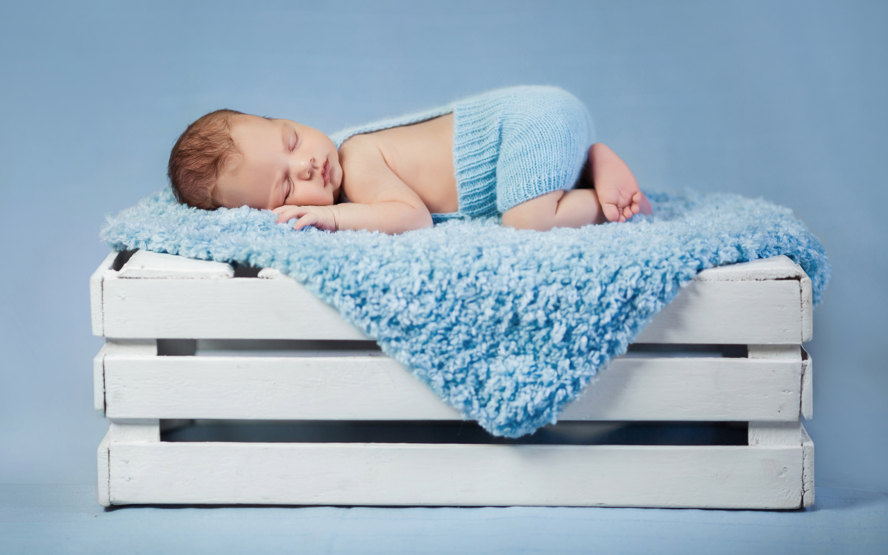 Маленький грудной ребенок спит на синем покрывале на деревянном ящике