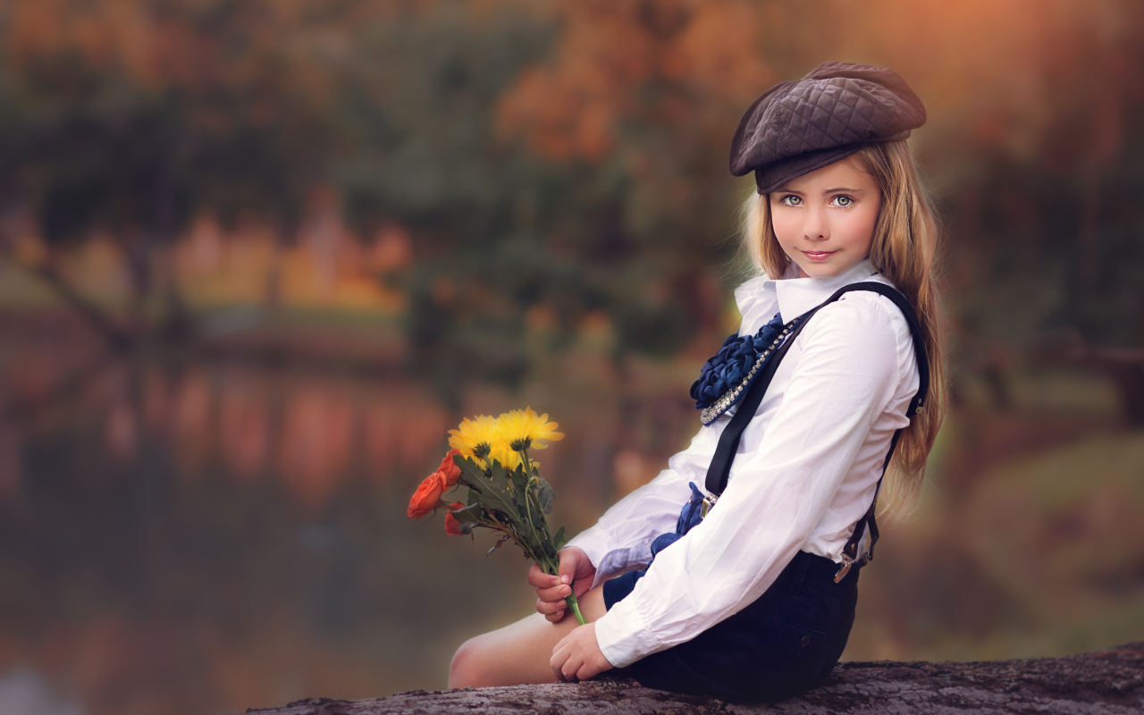 Красивая девочка в кепке с букетом в руках сидит на дереве