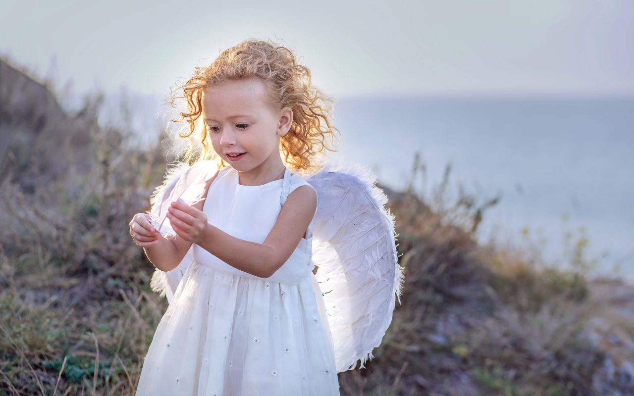 Красивая маленькая девочка в белом платье с крыльями ангела