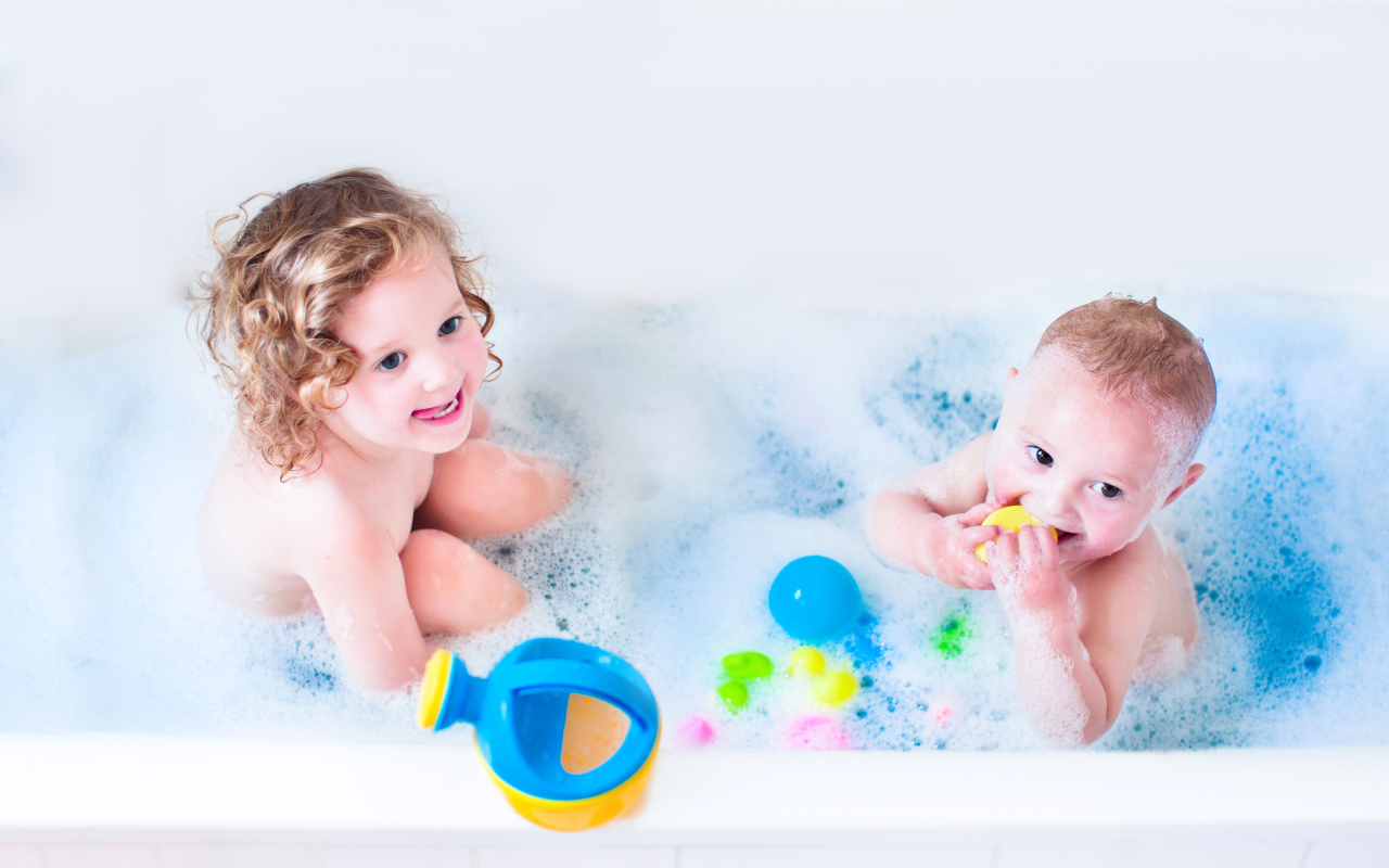 Маленькие мальчик и девочка купаются в ванной с игрушками