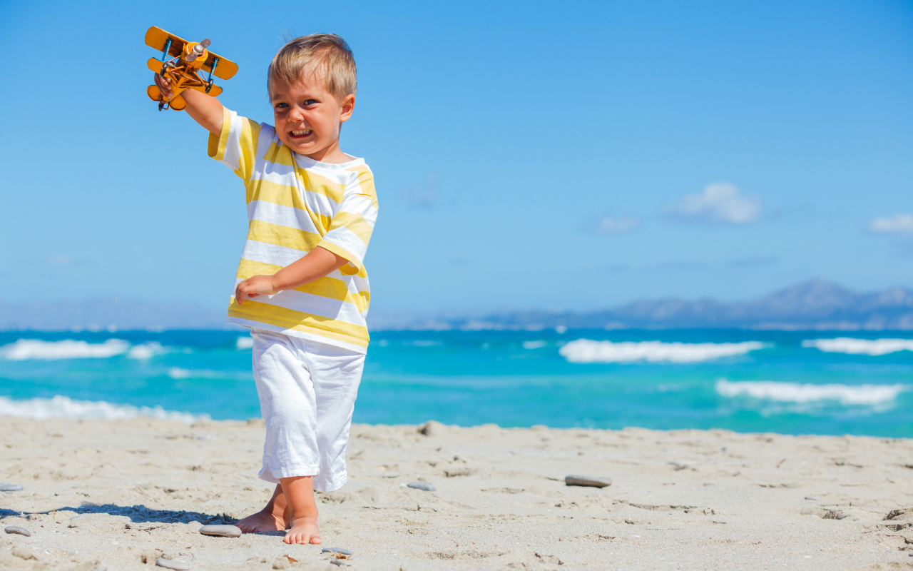 Маленький мальчик на пляже с игрушечным самолетом в руках